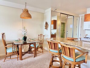 A dining area with a glass-top table, wicker chairs, and a hanging light fixture. - Junior Suite Oceanfront #907 (Lahaina)