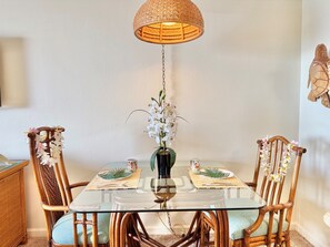 Comedor con mesa de vidrio, sillas de mimbre y lámpara colgante.
