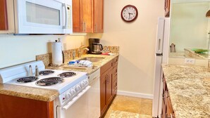 A kitchen with wooden cabinets, a white stove, a microwave, a clock, and a coffee maker. - Junior Suite Oceanfront #907 (Lahaina)