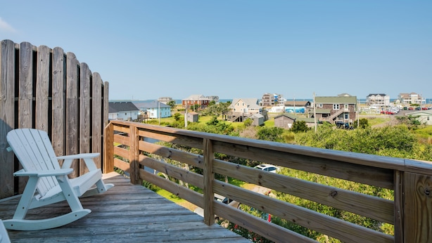 A wooden deck with a rocking chair and a wooden railing overlooking a coastal town. - Quiet Hatteras Duplex with Decks ~ 1 Mile to Beach (Hatteras)