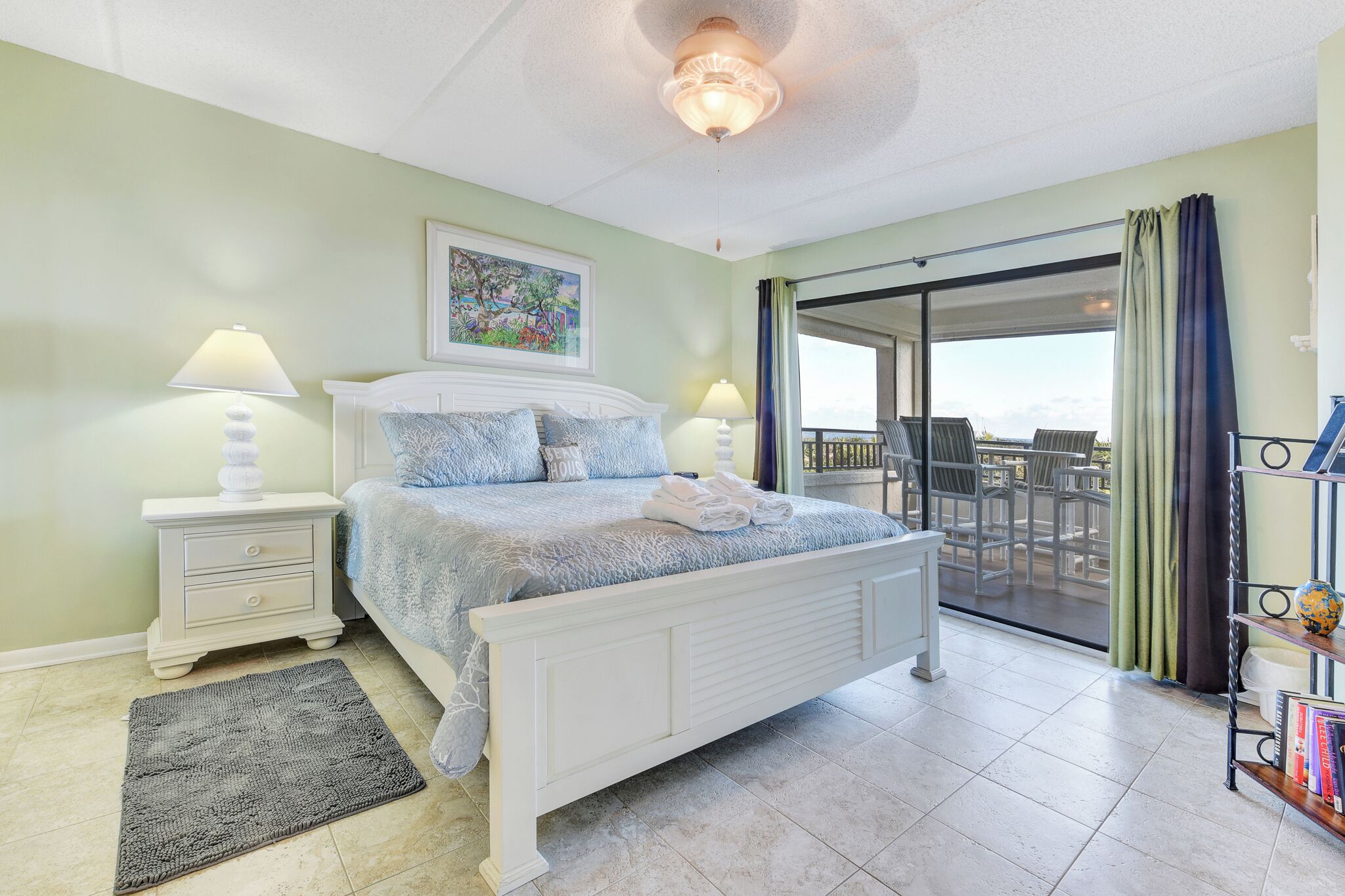 A bedroom with a bed, nightstands, a rug, a balcony with a view, and a bookshelf.