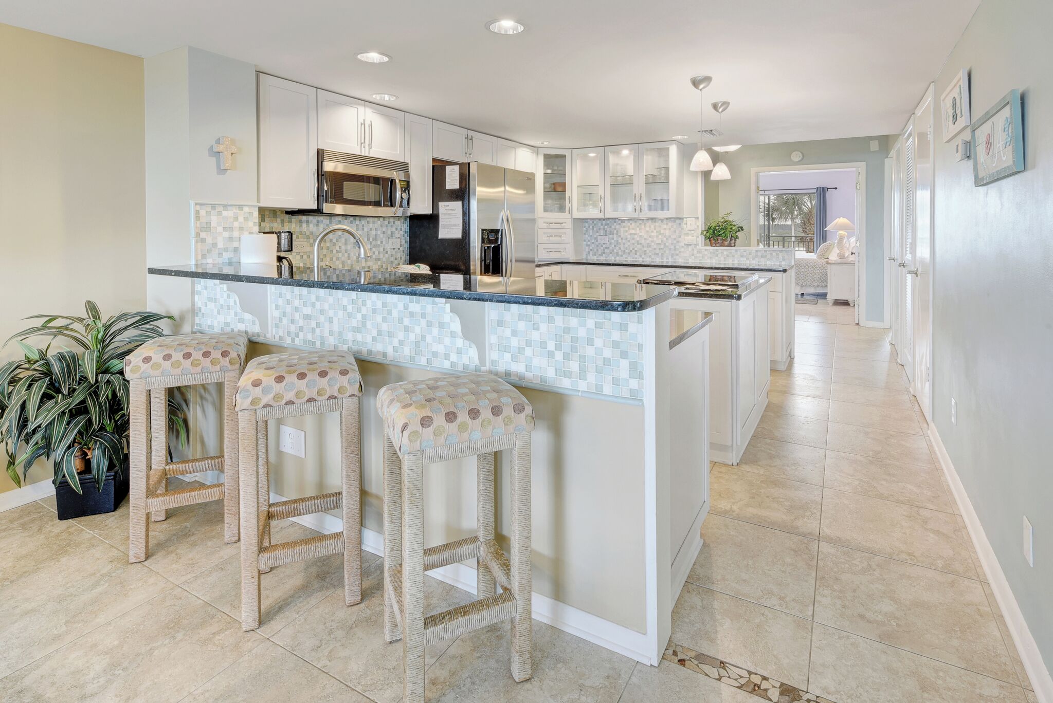 A modern kitchen with a central island, bar stools, and a potted plant.