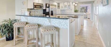 A modern kitchen with a central island, bar stools, and a potted plant.
