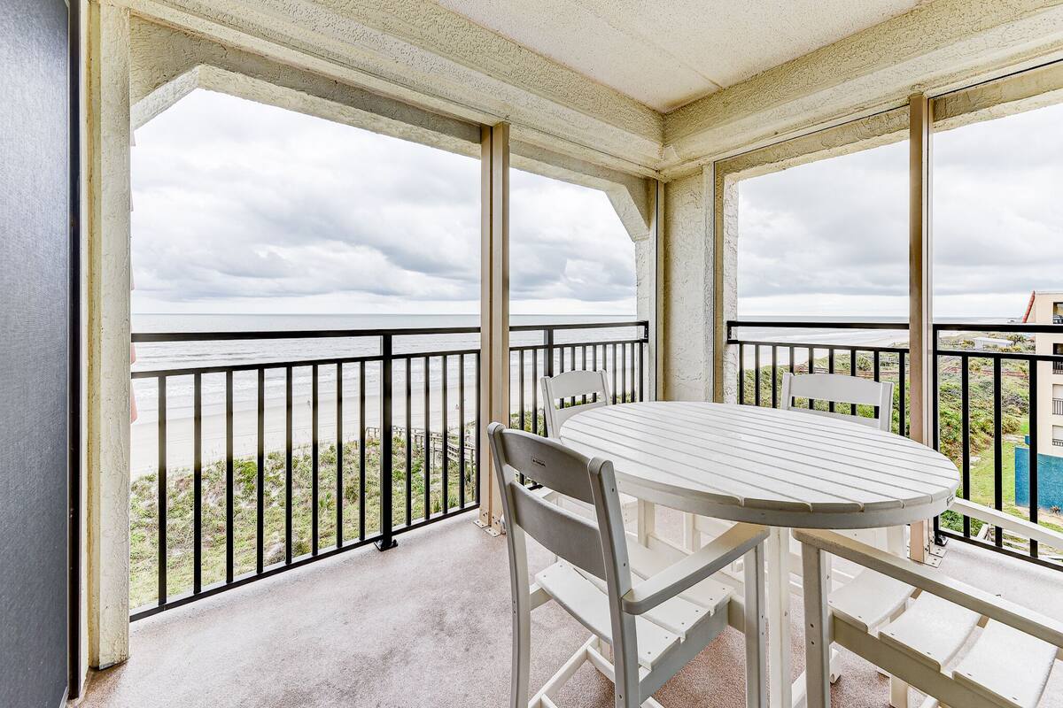 Ein überdachter Balkon mit Tisch und Stühlen mit Blick auf einen Strand.