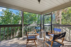 Une terrasse extérieure couverte, dotée de chaises et d’une table en bois, et entourée de panneaux de verre offrant une vue sur la verdure.