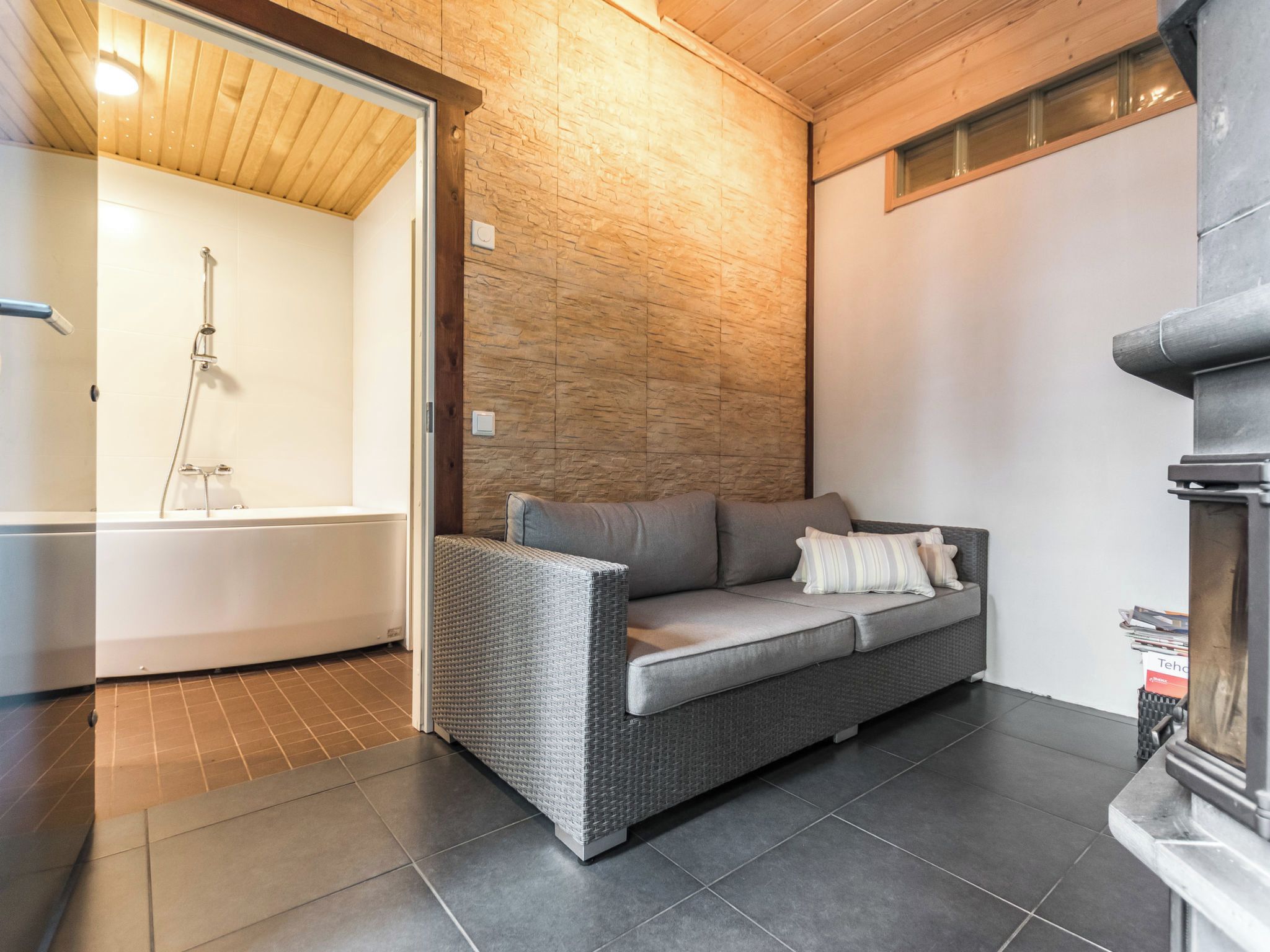 A modern bathroom with a shower, a grey sofa with cushions, and a tiled floor.