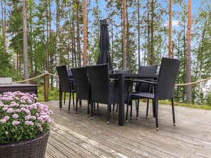Un área de comedor al aire libre con una mesa y sillas, rodeada por una terraza de madera y altos árboles.