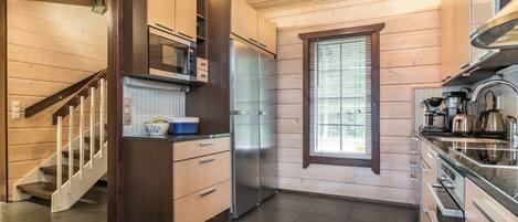 A modern kitchen with wooden cabinetry, a stainless steel refrigerator, and a window with blinds.