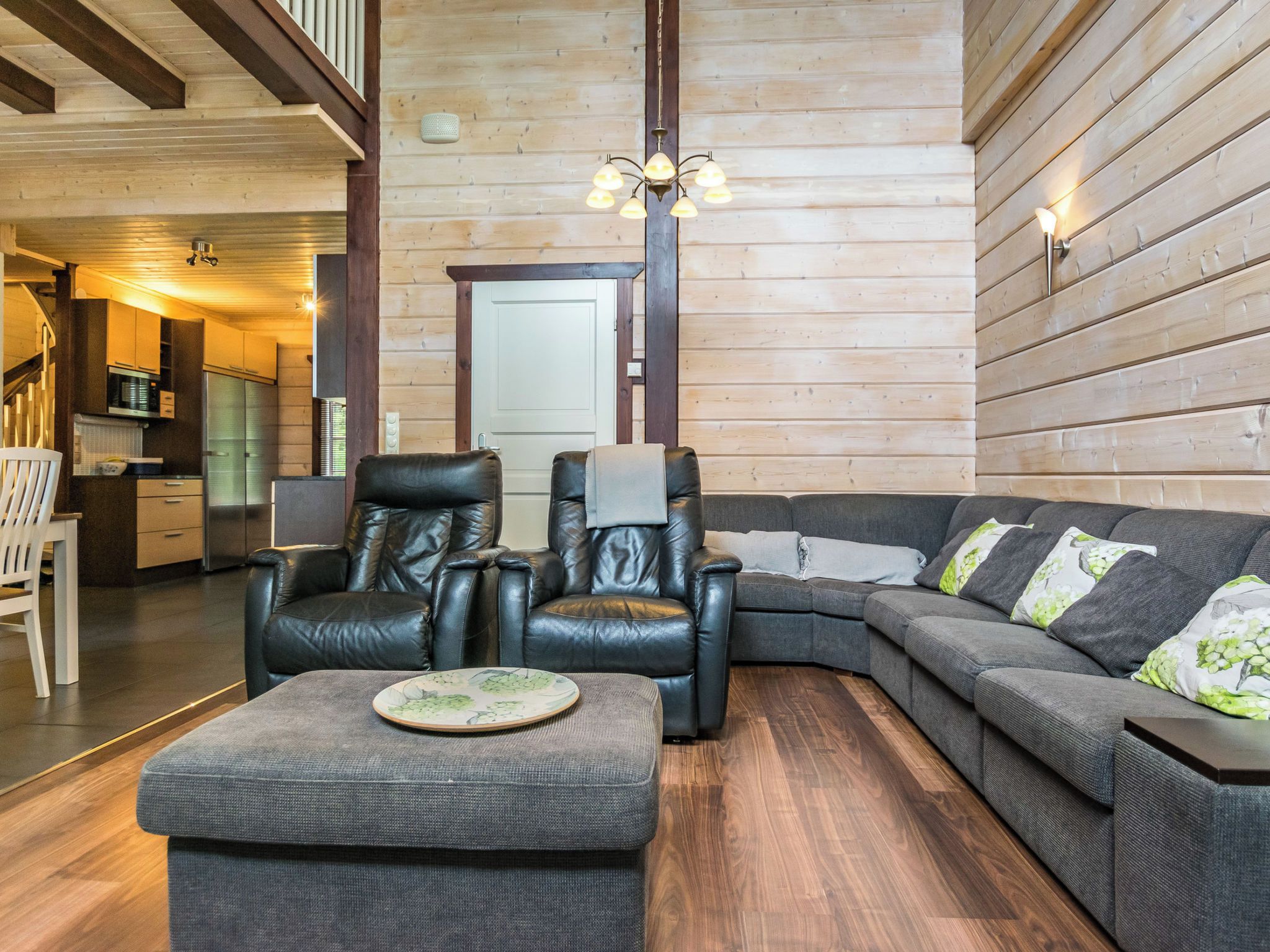 A modern living room with a sectional sofa, two leather armchairs, a small ottoman, and a dining table.