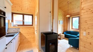 A compact wooden cabin with a kitchenette, a black stove, a blue sofa, and a window providing natural light. - Chalet Stressless I by Interhome (Presseggen)