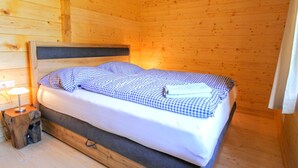 A wooden cabin room with a bed, a nightstand, and a lamp. - Chalet Stressless I by Interhome (Presseggen)