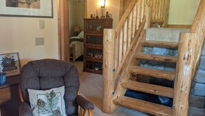 Een gezellige woonkamer met een houten trap, een comfortabele fauteuil en een boekenplank.