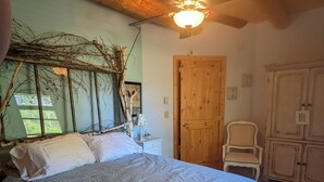 Een slaapkamer met een groot bed, houten balken in het plafond, een plafondventilator, een houten deur en een kledingkast.