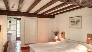 A bedroom with a large bed, wooden beams on the ceiling, a bedside table with a lamp, and a picture on the wall. - Authentic gîte on estate with swimming pool (Issac)