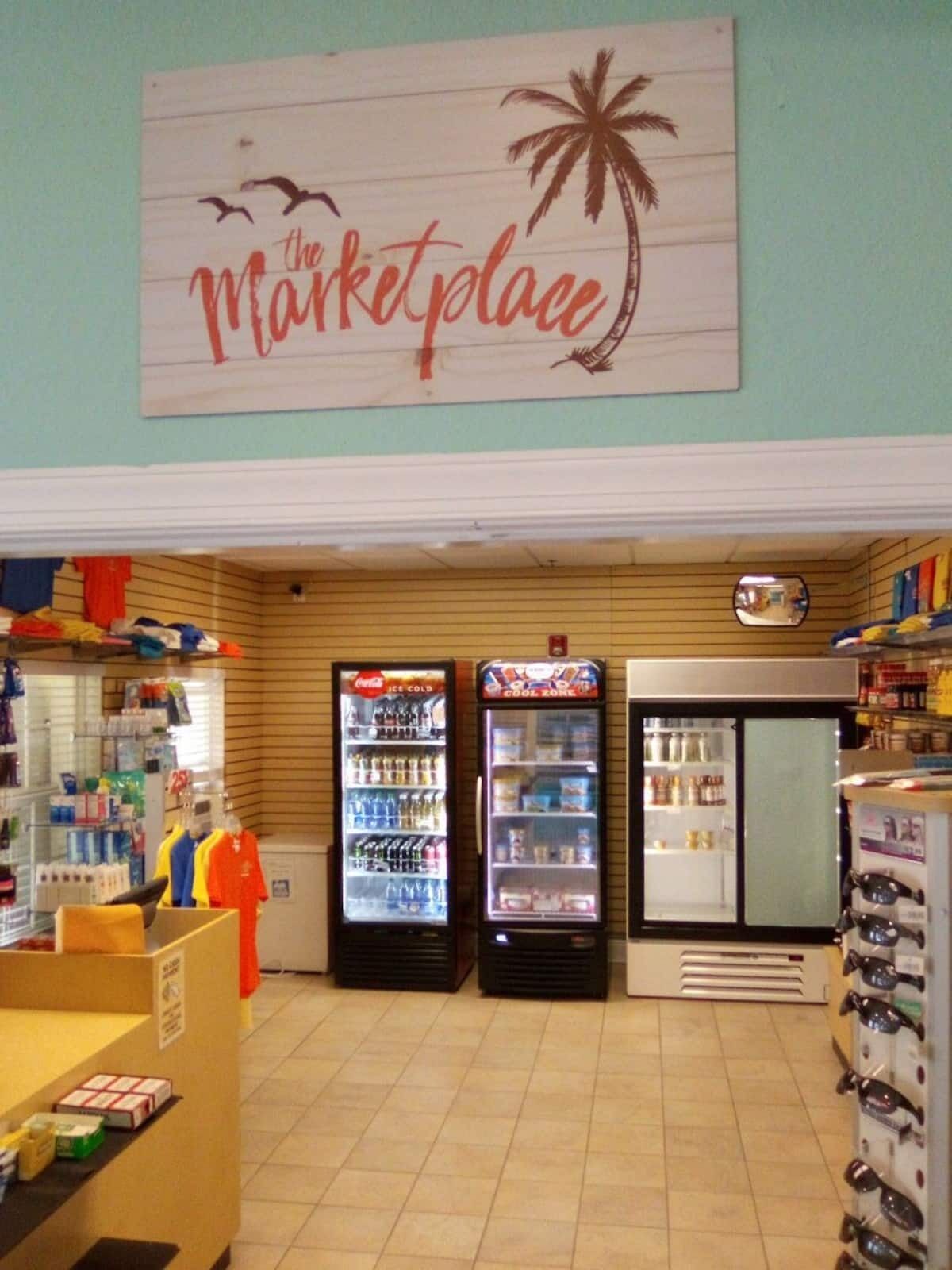Interior de una tienda con un letrero que dice 'Marketplace', máquinas expendedoras y estantes llenos de diversos productos.