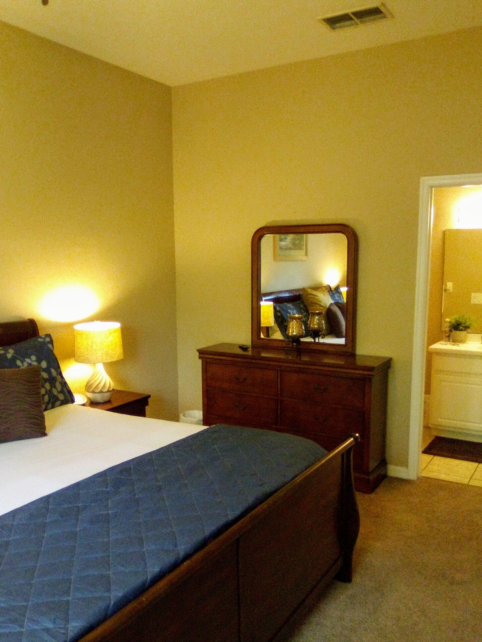 A hotel room with a bed, a dresser, a mirror, and a nightstand with a lamp.
