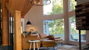 Amplia sala de estar con techo de madera, ventanas grandes, chimenea y una disposición de asientos acogedora.