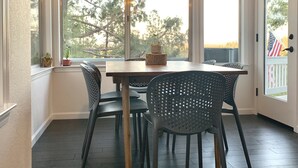 Un comedor con mesa y sillas de madera, ventanas amplias y una lámpara colgante.