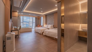Habitación de hotel moderna con dos camas, un ventanal grande con vista a la ciudad, un escritorio con silla y un baño con lavamanos y espejo.