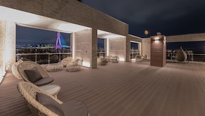 Una terraza en la azotea con mobiliario de mimbre, vistas a un horizonte urbano y una estructura de edificio moderna.