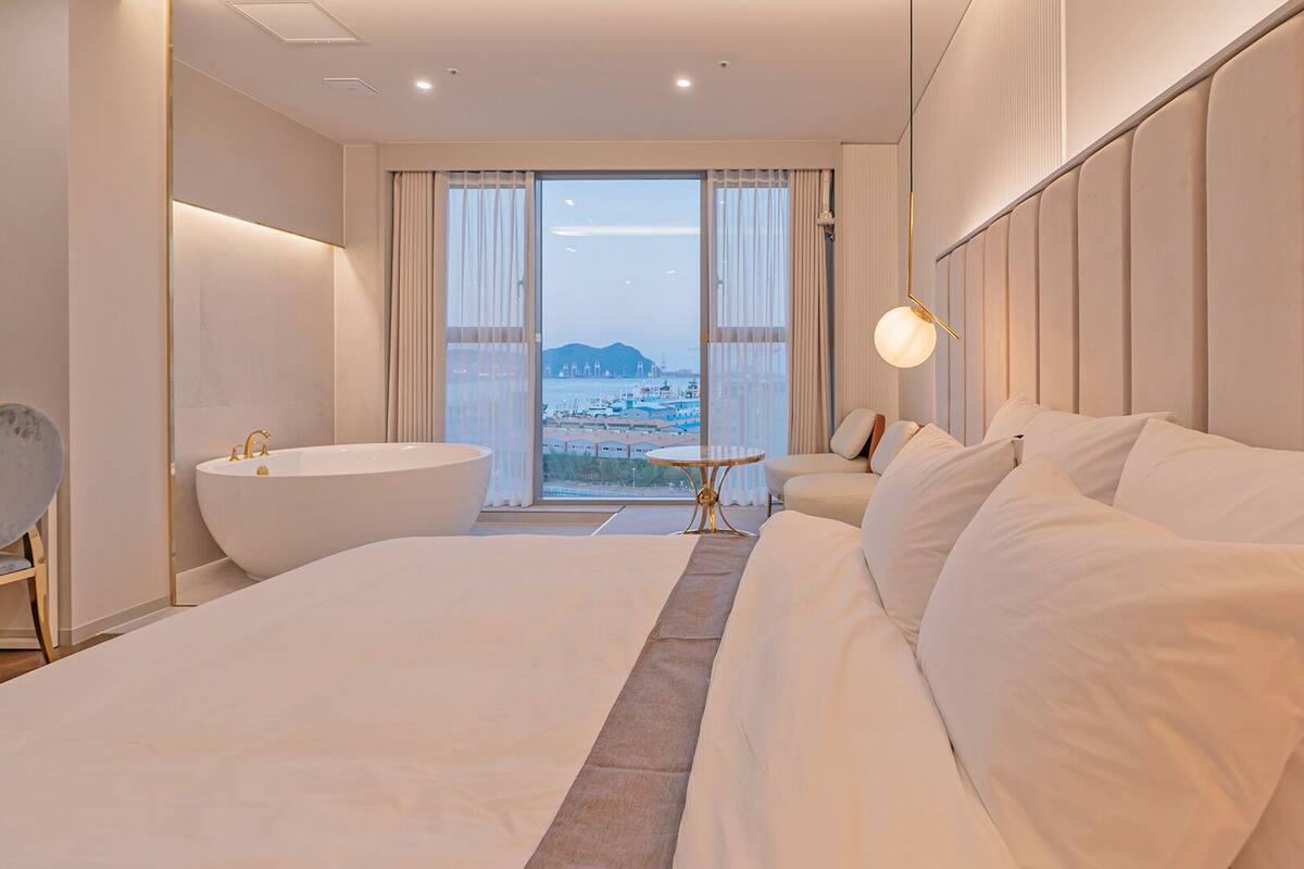 Un hotel moderno con una cama grande, una bañera, una mesa redonda y vista al mar.