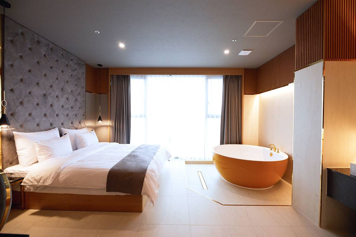 Una habitación de hotel moderna con una cama grande, una bañera y un ventanal que proporciona luz natural.