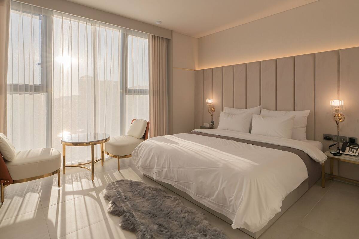Una habitación de hotel moderna con una cama grande, una mesa redonda, dos sillas, un tapete mullido y un teléfono en una mesita de noche.