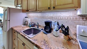 Una cocina con armarios de madera, encimera de granito, cafetera y un juego de cuchillos.