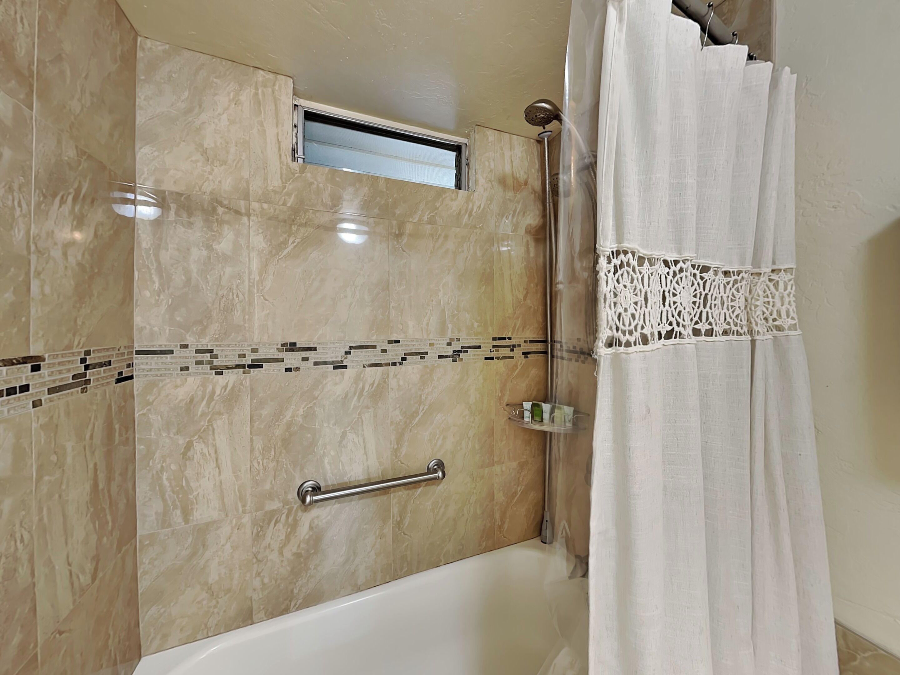 A bathroom with a shower, a handrail, and a tiled wall.