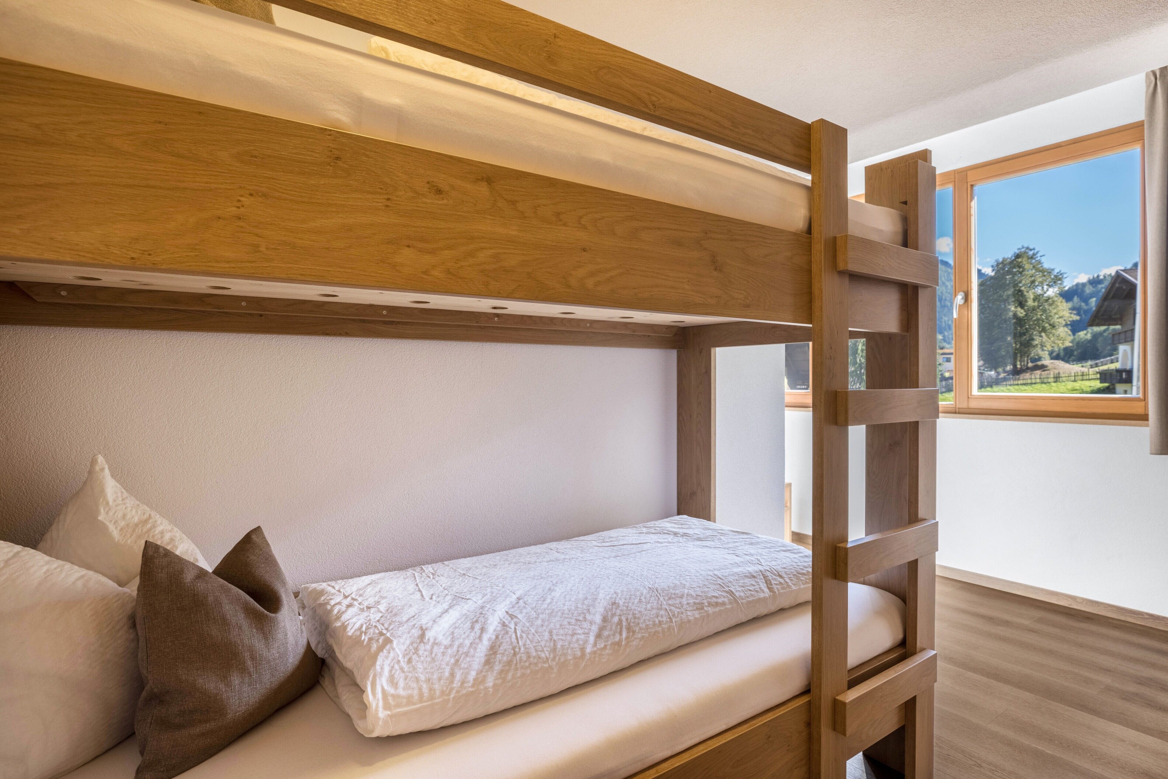 Un lit superposé avec une échelle en bois, du linge de lit blanc et des oreillers.