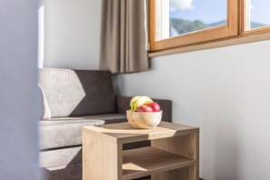 Une petite table d’appoint en bois, sur laquelle se trouve un saladier rempli de fruits, dans une pièce où l’on aperçoit un canapé et une fenêtre.