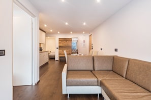 A modern interior with a sofa, wooden flooring, a kitchen area, and a dining table.