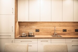 Una cucina moderna con mobili bianchi, zoccolo in legno, elettrodomestici in acciaio inossidabile e un lavello a due vasche.