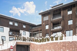 A multi-story building with balconies, a stone wall, and a snow-covered ground.