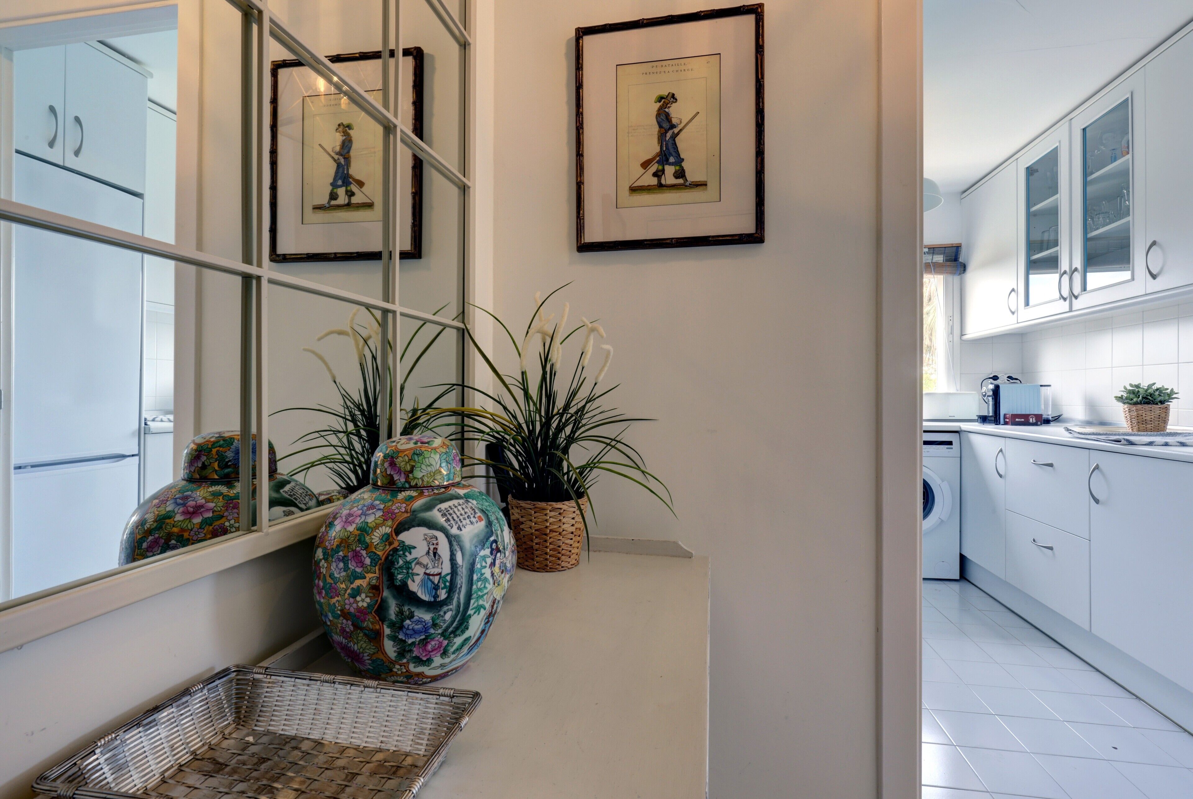 Cocina moderna con armarios blancos, lavadora y elementos decorativos como un florero y cuadros enmarcados.