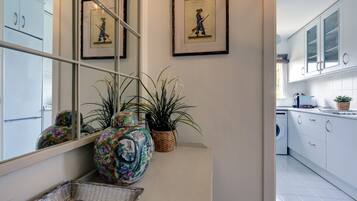 Cocina moderna con armarios blancos, lavadora y elementos decorativos como un florero y cuadros enmarcados.
