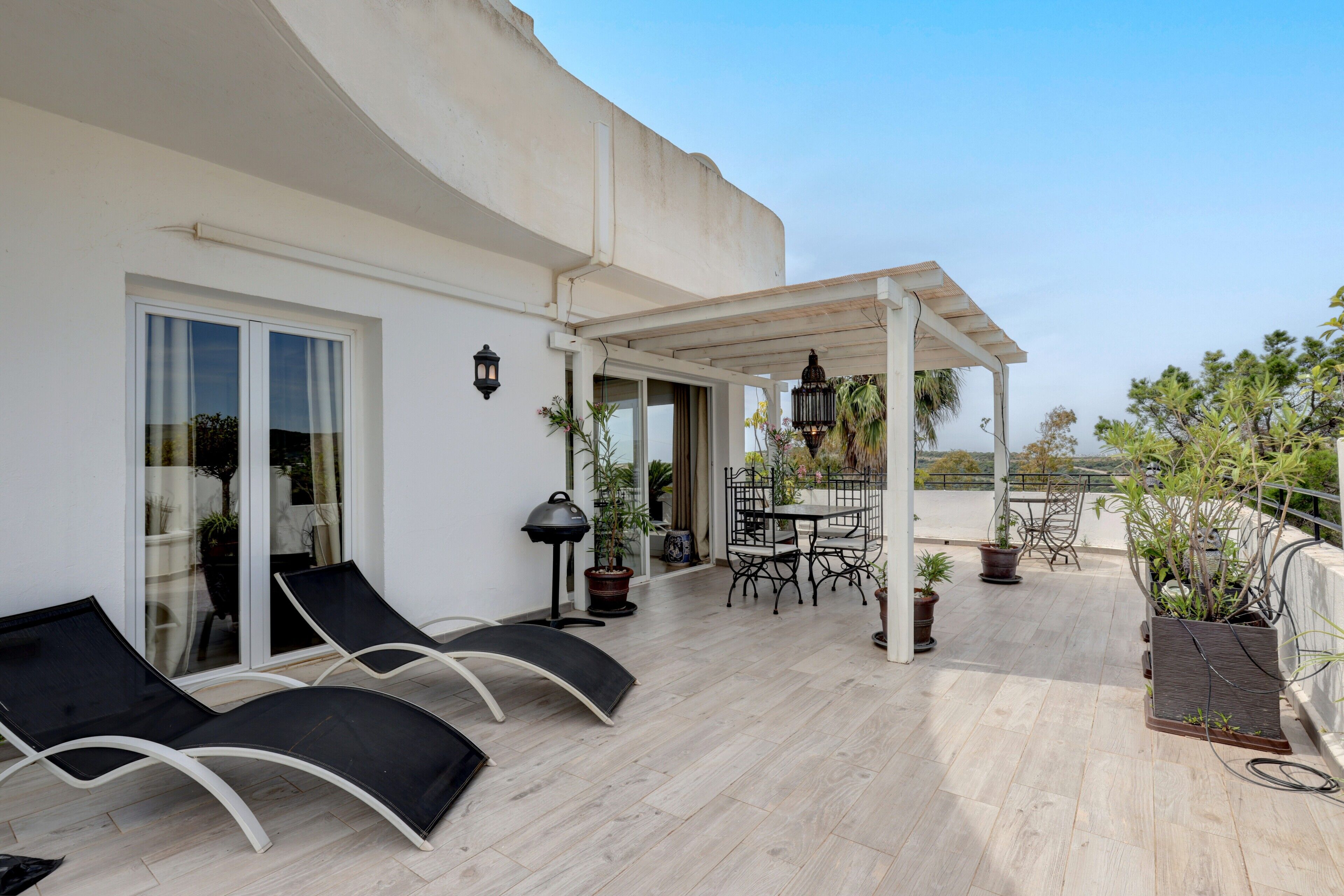 A covered outdoor area with lounge chairs, a table, and potted plants.
