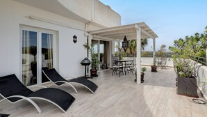 A covered outdoor area with lounge chairs, a table, and potted plants. - Apartamento "Del Paraíso" with Mountain View, Shared Pool and Private Terrace (Estepona)