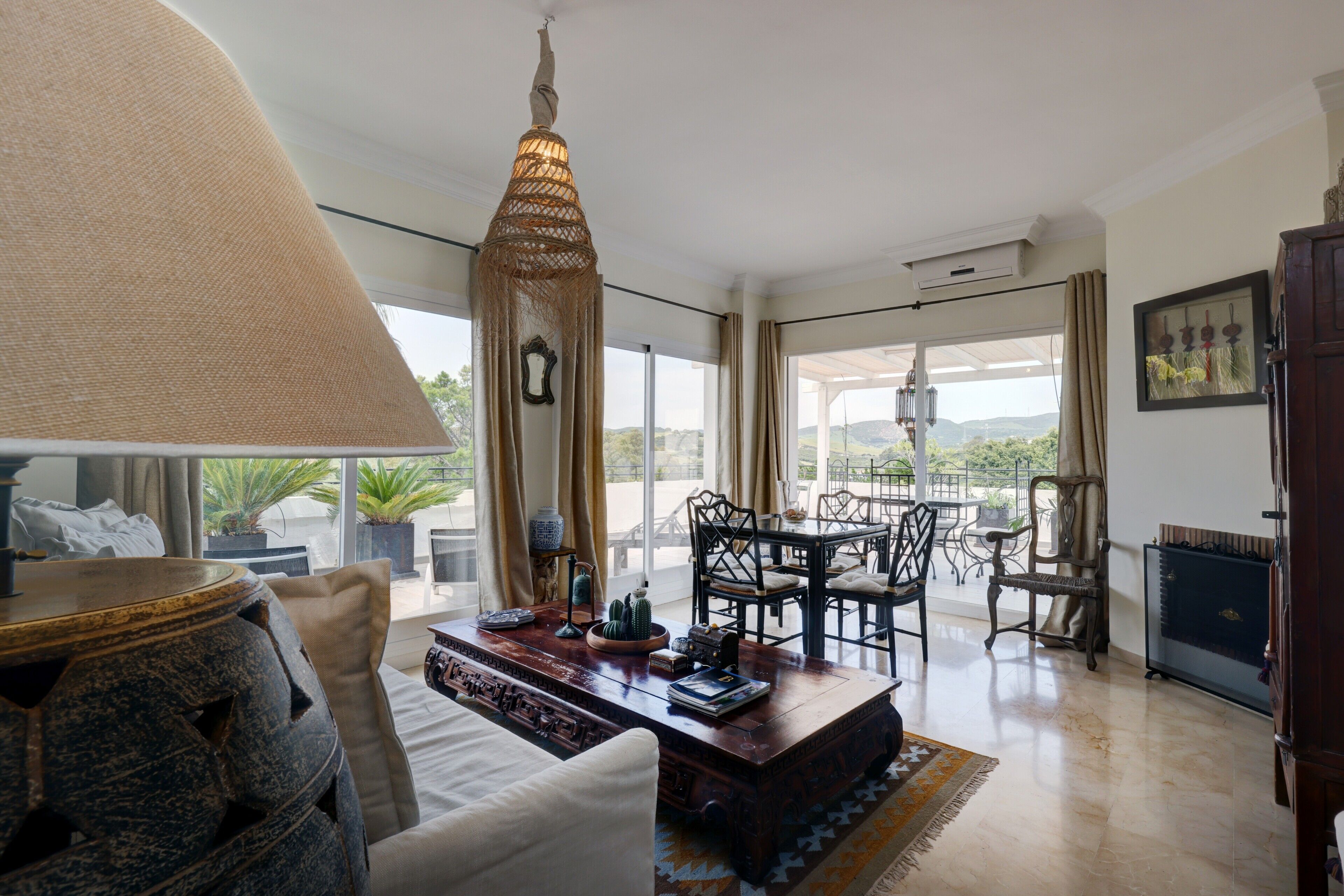 A spacious living area with a large window, a dining table, and a decorative lamp.