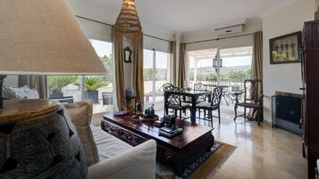 A spacious living area with a large window, a dining table, and a decorative lamp.