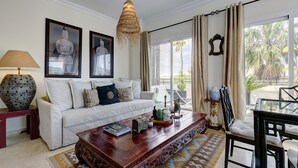 A living room with a white sofa, a wooden coffee table, a hanging light fixture, and a view of palm trees through the window. - Apartamento "Del Paraíso" with Mountain View, Shared Pool and Private Terrace (Estepona)