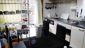 A compact kitchen with a stove, sink, and shelves with pots and pans. - Tuwano sou (Tsuwano)