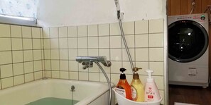 Une salle de bain équipée d’une baignoire, d’un lave-linge et d’un seau contenant des articles de toilette.