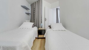 A modern hotel room with two single beds, a small table, a chair, and a window with curtains. - Chic and spacious apart with parking (Saint-Germain-en-Laye)