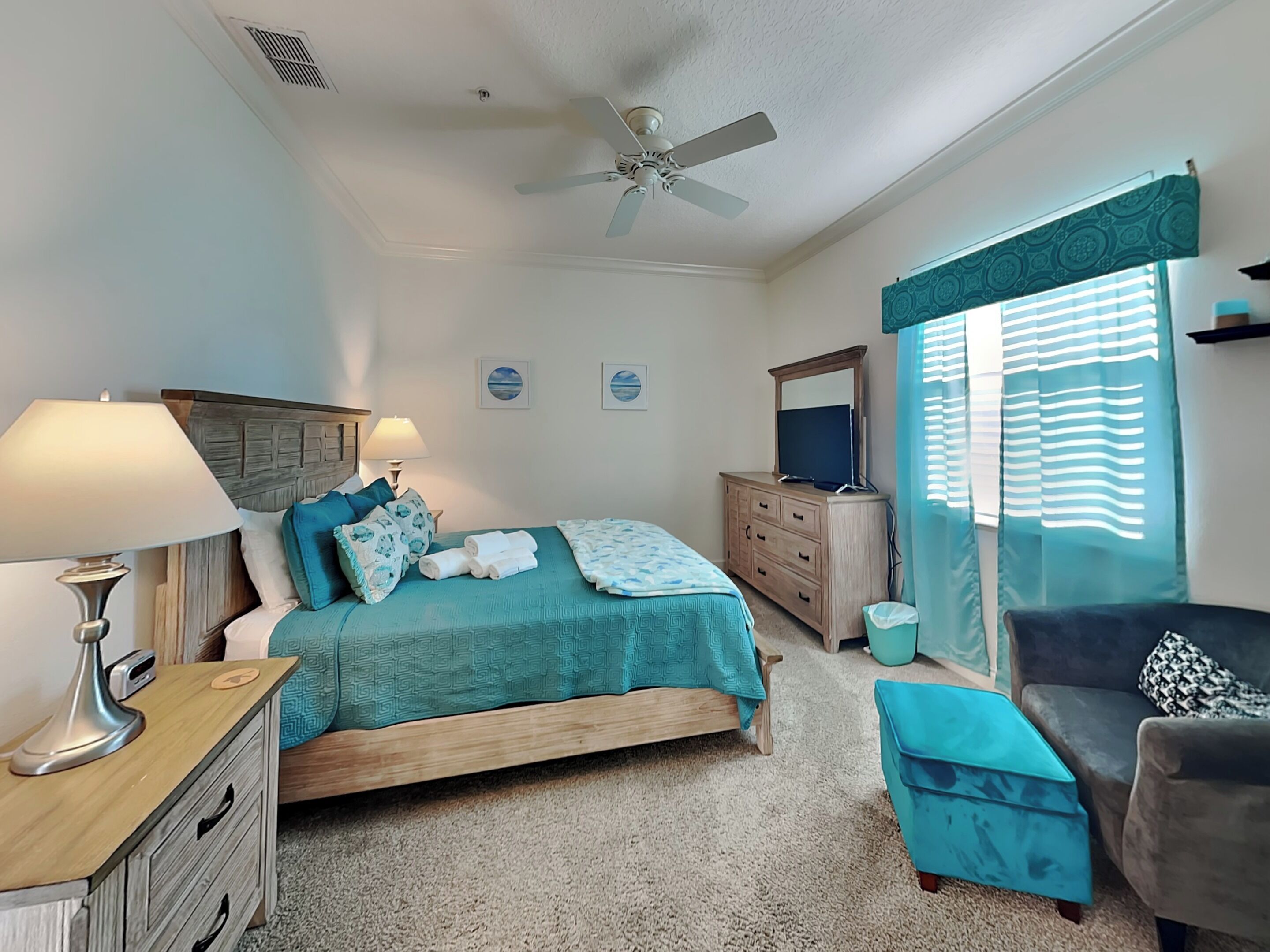 Une chambre à coucher comprenant un lit, une commode, une coiffeuse, une chaise et un ventilateur de plafond.