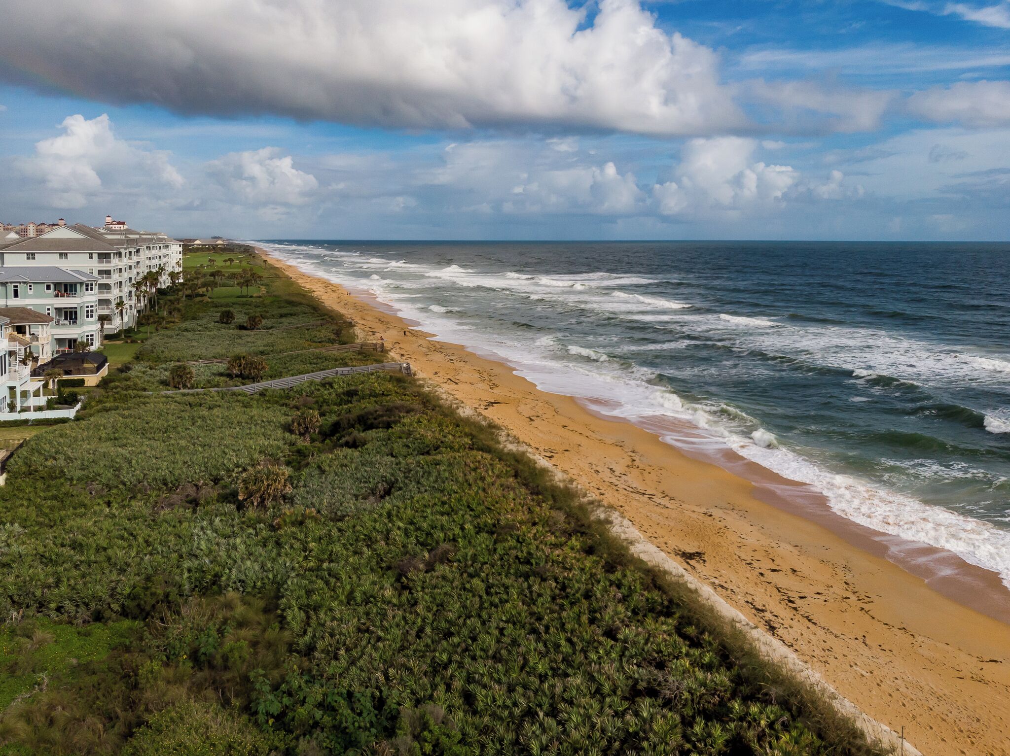 A coastal view with a beach, ocean waves, and a row of beachfront houses.