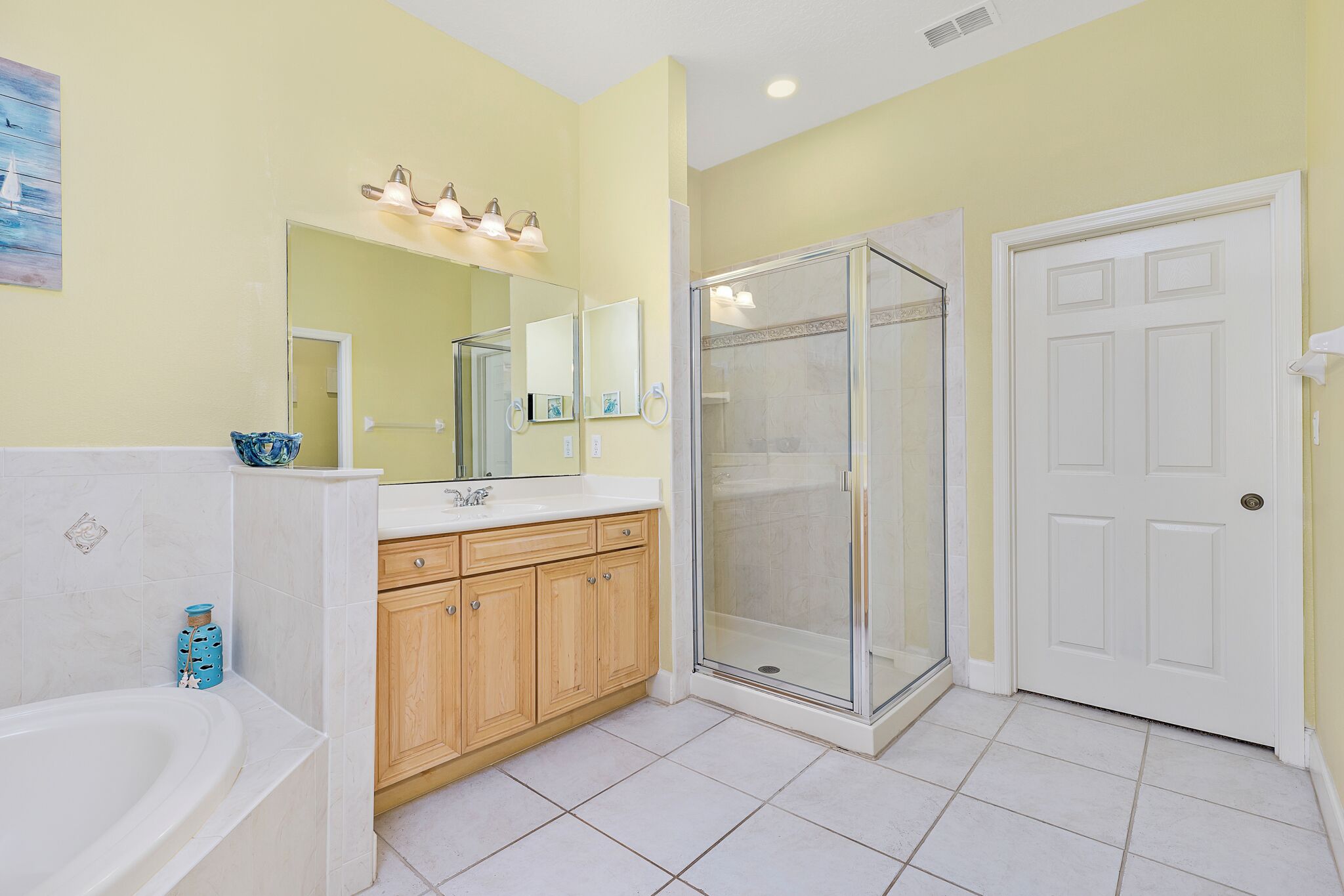A bathroom with a bathtub, wooden vanity, glass shower enclosure, and a white door.