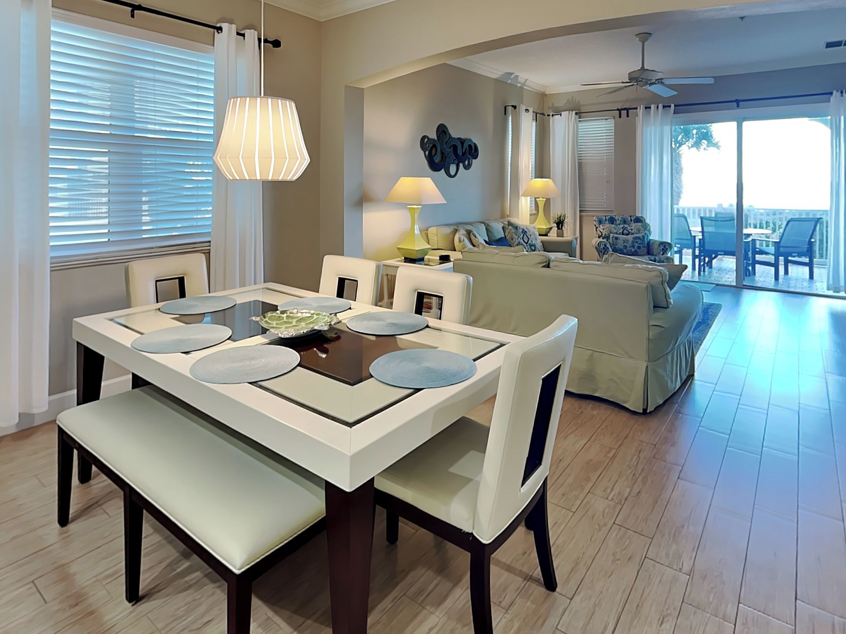 A dining area with a table set for four, a sofa, and a ceiling fan in a bright living space.