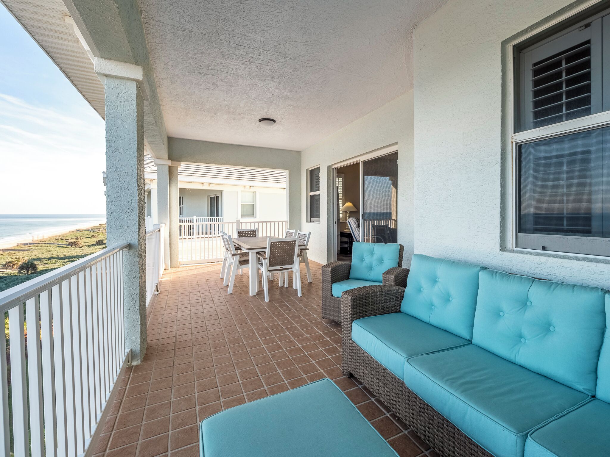 A covered patio with a dining table and chairs, a sofa, and a view of the beach.