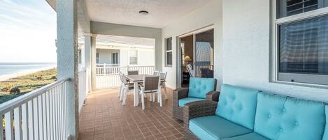 A covered patio with a dining table and chairs, a sofa, and a view of the beach.